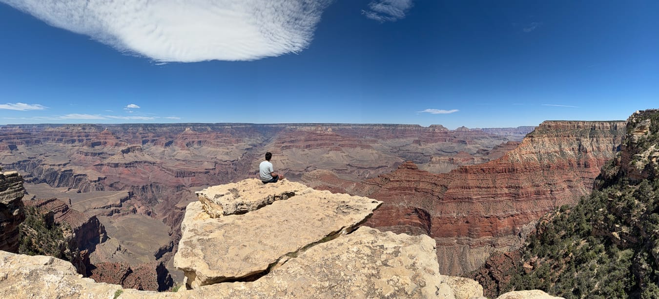 Panorama of the Grand Canyon with a figure sitting on a rock ledge