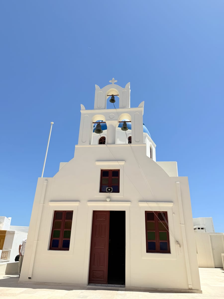 A cream church with a triple bell tower against blue sky