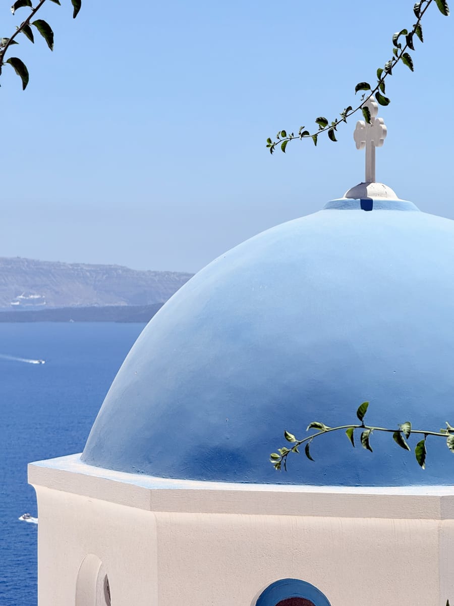 A blue church dome with a cross above the sea