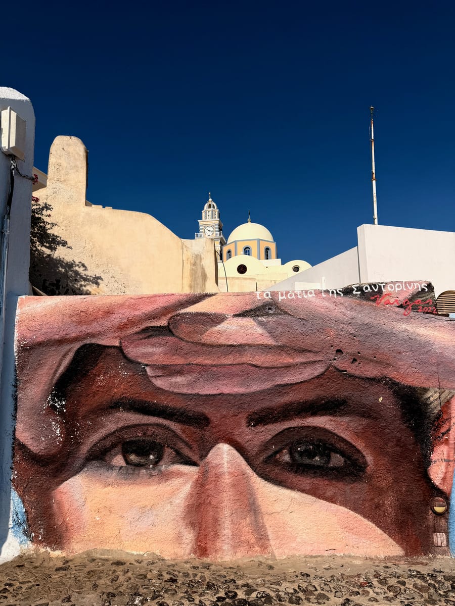 A painted pair of eyes on a wall below a hillside church